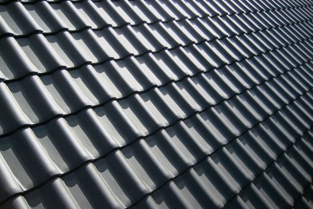 Close-up of dark grey profiled roof tiles casting crisp shadows in bright sun