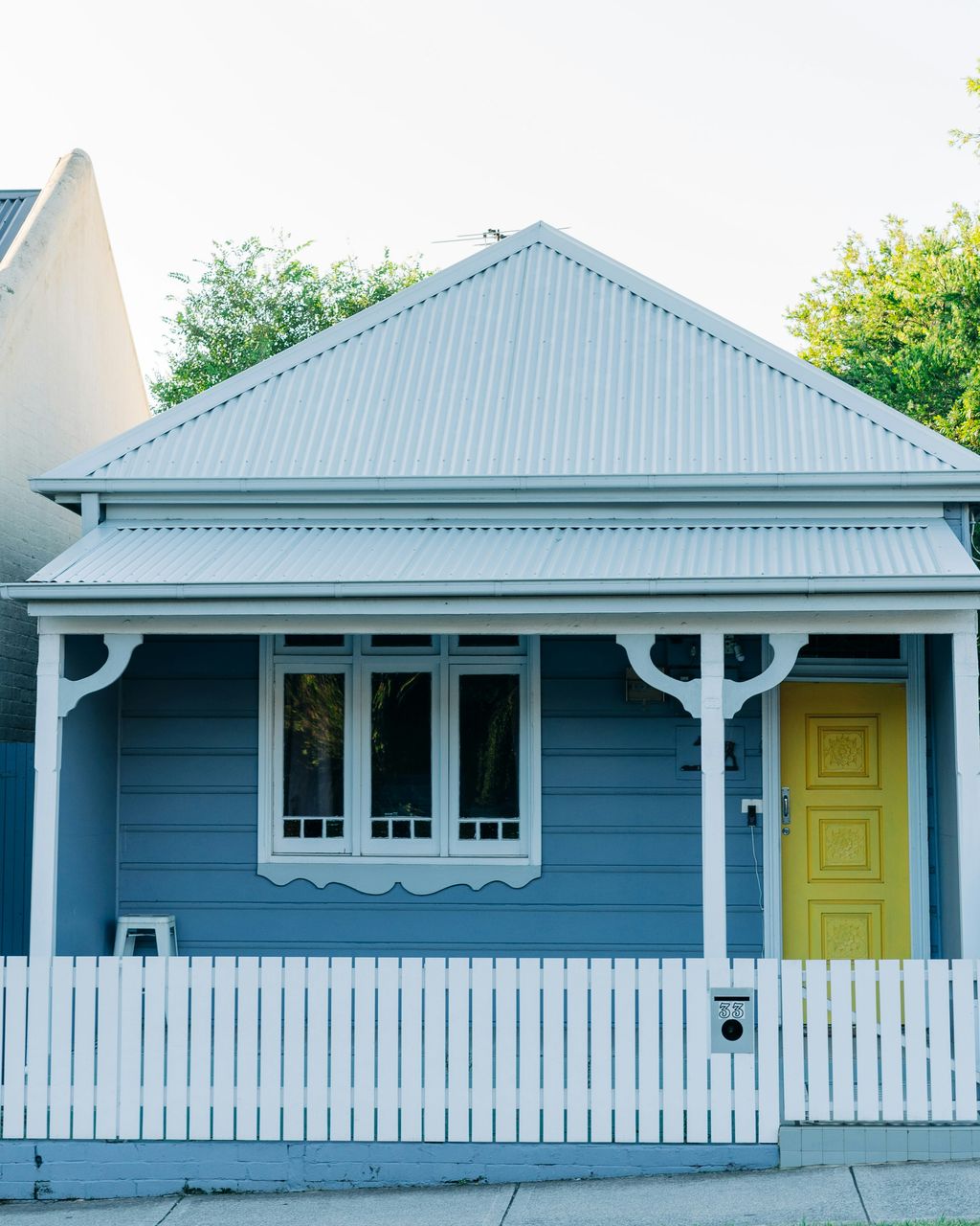 Blue weatherboard cottage with a pale corrugated Colorbond hip roof, white verandah and picket fence in Leichhardt, Sydney