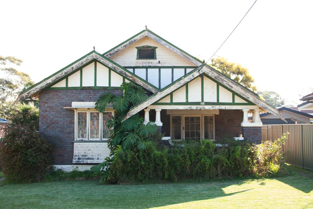 Brick Californian bungalow with twin green-trimmed gables and a leafy front garden in Revesby, Sydney