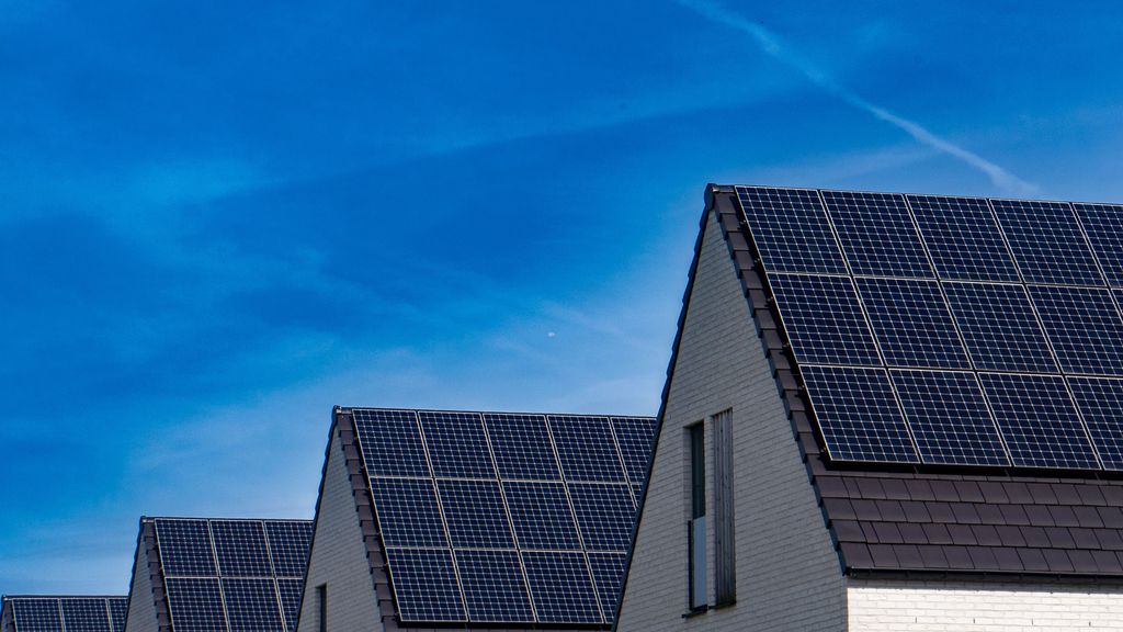 Rows of dark solar panels on steep gabled residential roofs under a bright blue sky