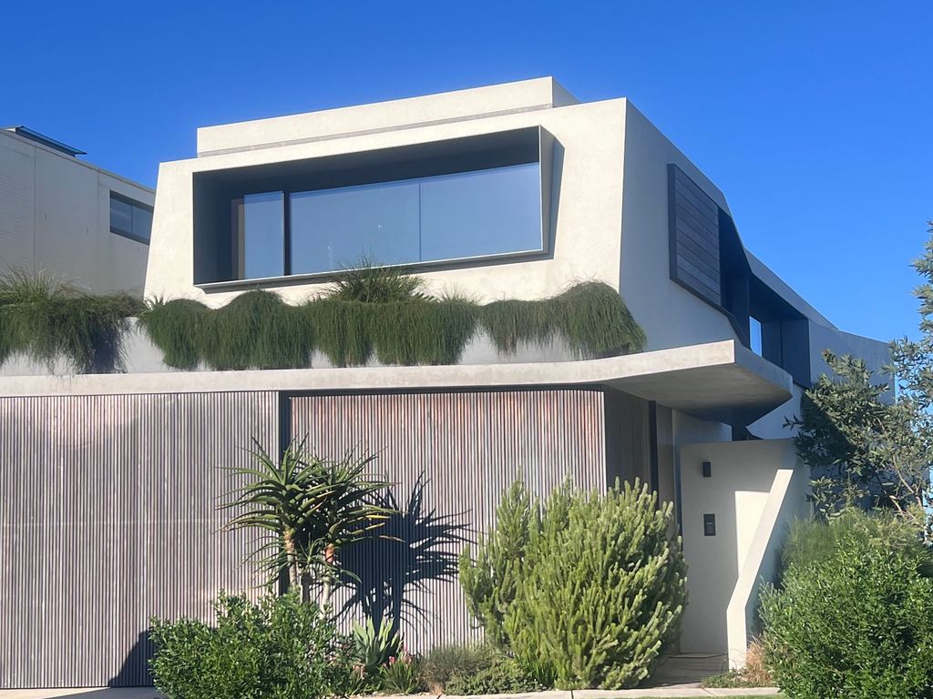 Modern two-storey home with a smooth rendered facade, timber battens and native garden under a clear sky in Sydney